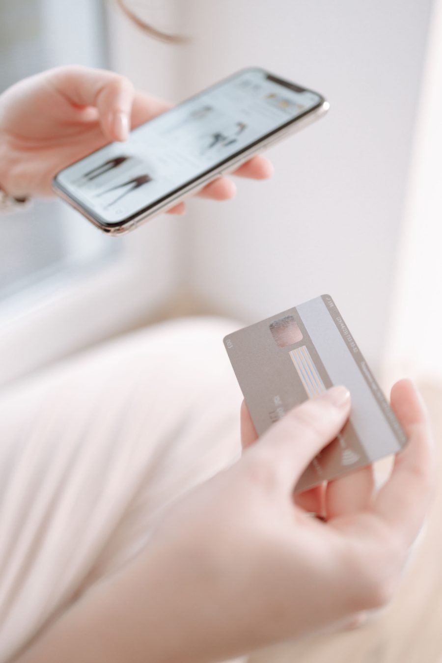 A person holding a phone in one hand and a payment card in the other.